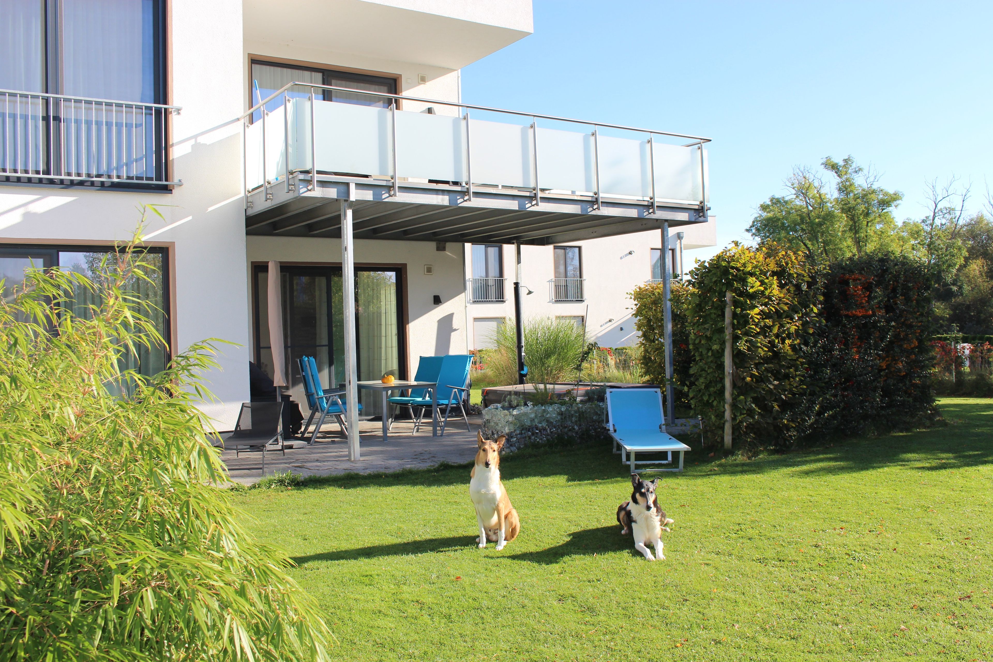 Ein modernes, zweistöckiges Gebäude mit überdachter Terrasse, Gartenmöbeln und einem gepflegten Rasen.