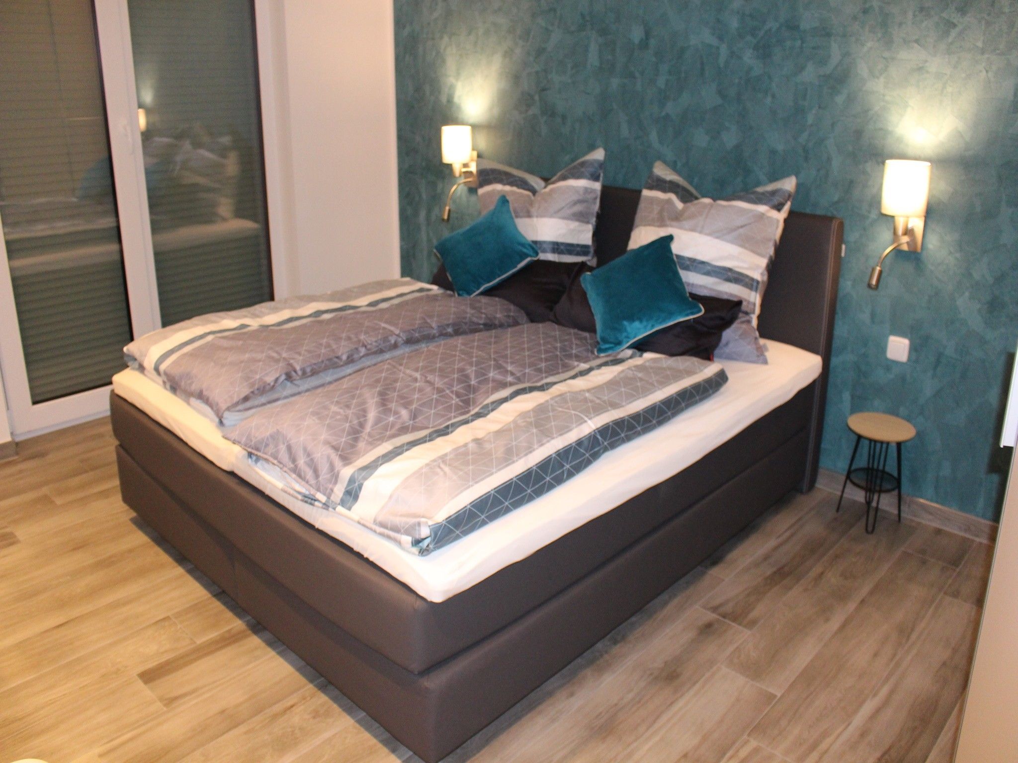 Ein modernes Schlafzimmer mit einem großen Bett, einem kleinen Hocker und zwei Wandleuchten.