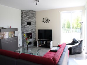 Ein modernes Wohnzimmer mit Kamin aus Stein, einem Flachbildfernseher, einem Glastisch und einem roten Sofa.