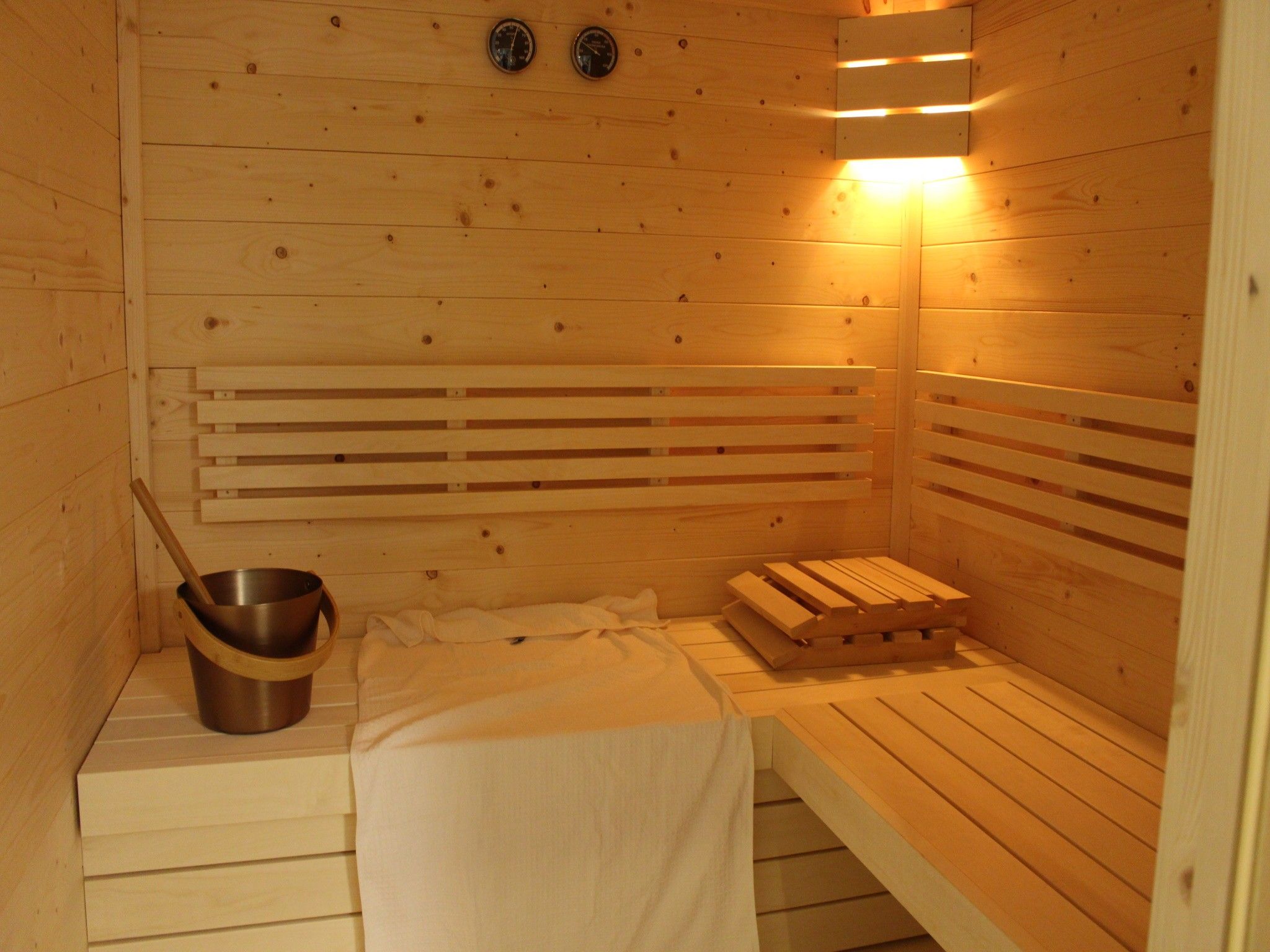 Un sauna avec des bancs en bois, un réchauffeur de banc et un seau.