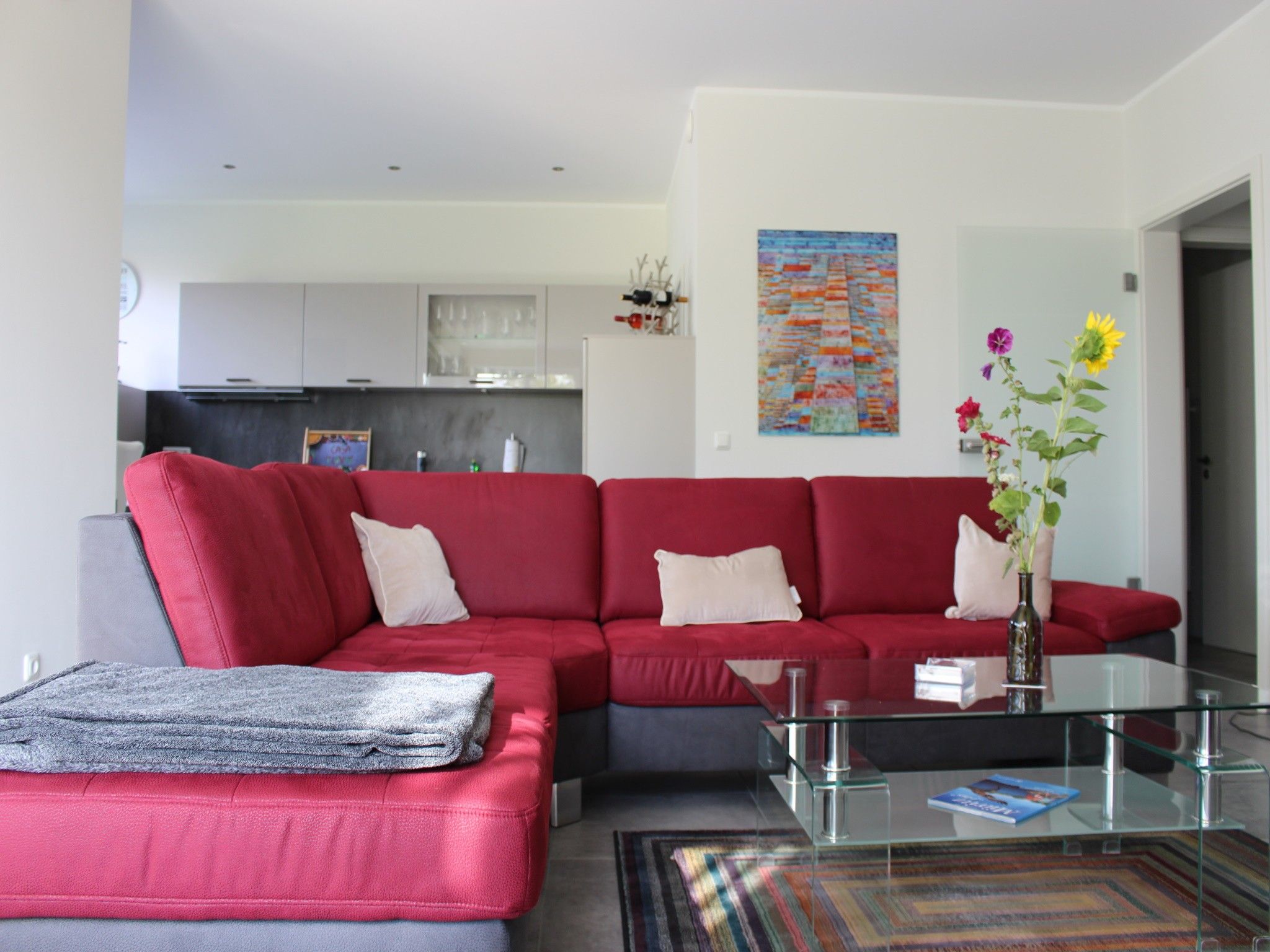 Un salon moderne avec un canapé d’angle rouge, une table basse en verre et un tapis à motifs.