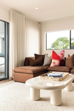 A modern living room with a sectional sofa, a coffee table, and a large window. - Marea by Khove - Kingscliff (Kingscliff)