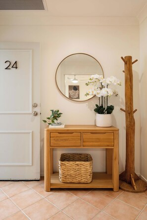 A wooden console table with a mirror, a potted orchid, and a wicker basket. - Marea by Khove - Kingscliff (Kingscliff)