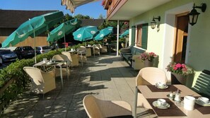 Une terrasse extérieure avec des tables et des chaises, des parasols et des plantes en pot.