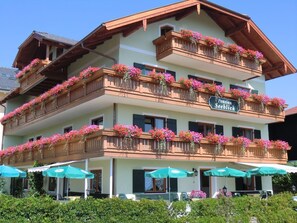 A multi-story hotel with balconies adorned with flowers, outdoor seating with umbrellas, and a sign indicating a restaurant. - 34-square-meter apartment with a balcony and a lake view (Gstadt am Chiemsee)
