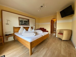 Een hotelkamer met een houten bed, een rode fauteuil, een aan de muur bevestigde televisie en een lijst met een foto.