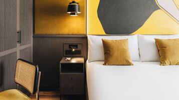 A hotel room with a bed, bedside table, chair, and a wall-mounted lamp.