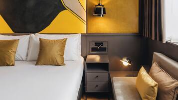 A hotel room with a bed, bedside table, lamp, and a wall-mounted control panel.
