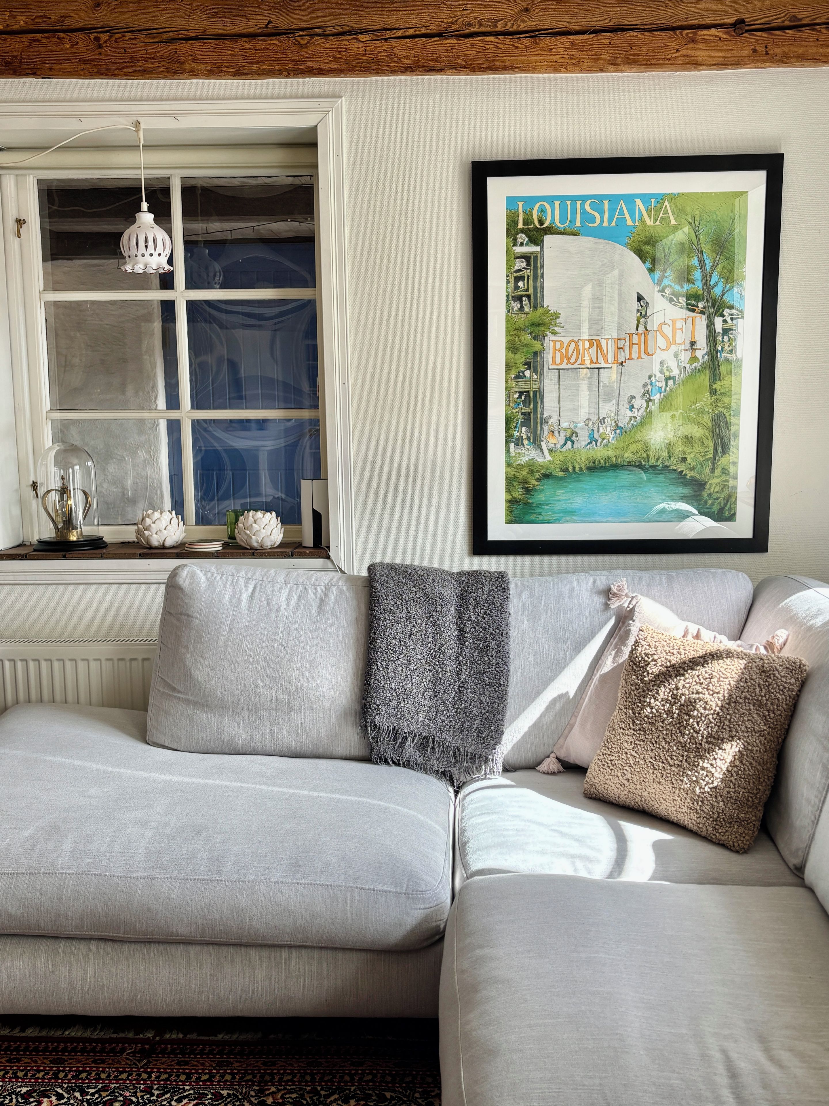 Een woonkamer met een bank, een lijst met een foto van een huis in Louisiana en een raam met een hanglamp.