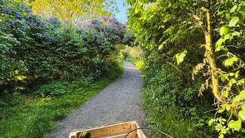 Ein Fahrrad mit einem Holzkorb vorne, abgestellt auf einem Schotterweg, umgeben von üppiger Vegetation und Bäumen.