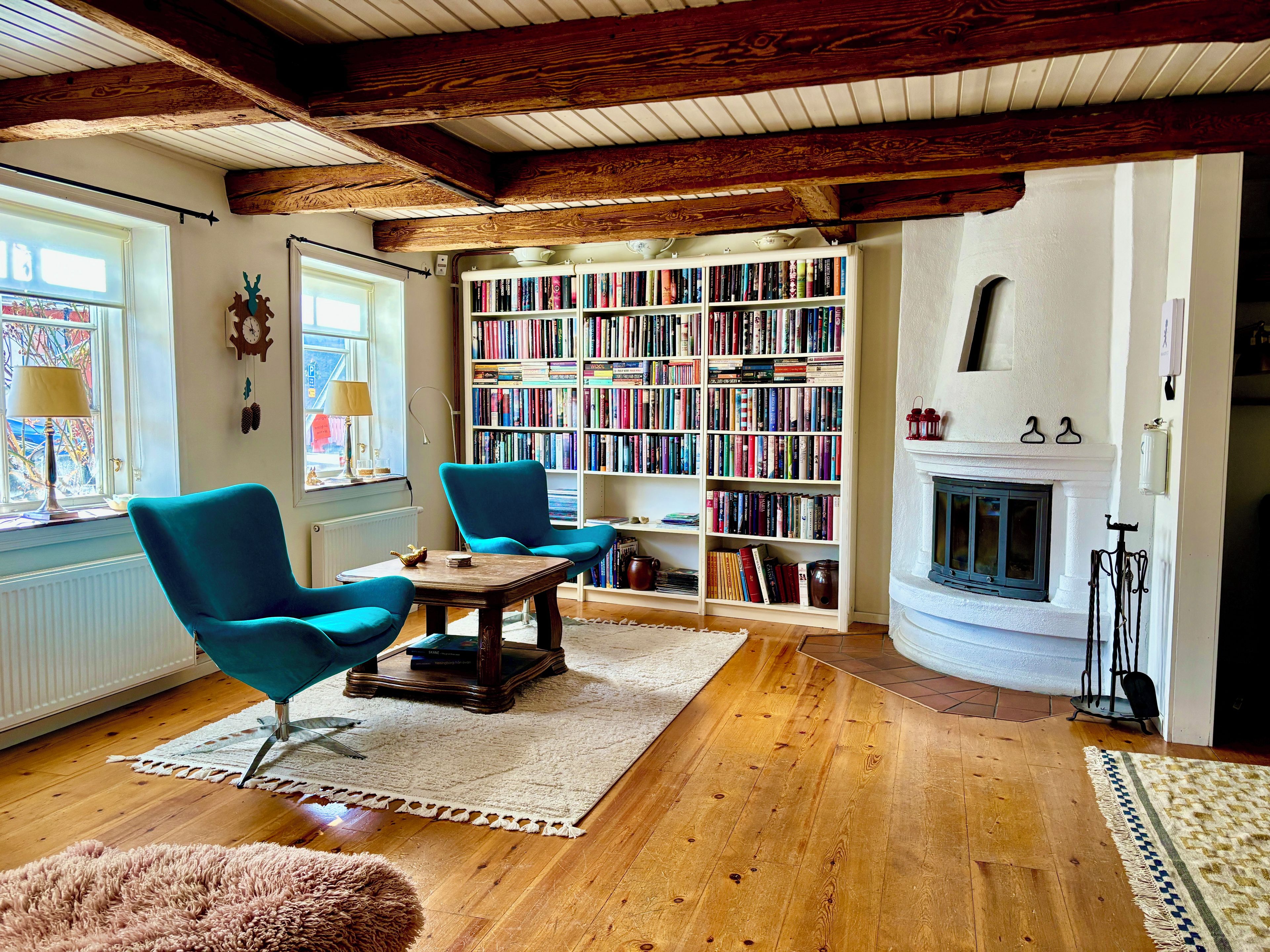 A cozy living room with a fireplace, wooden floors, and a large bookshelf filled with books.