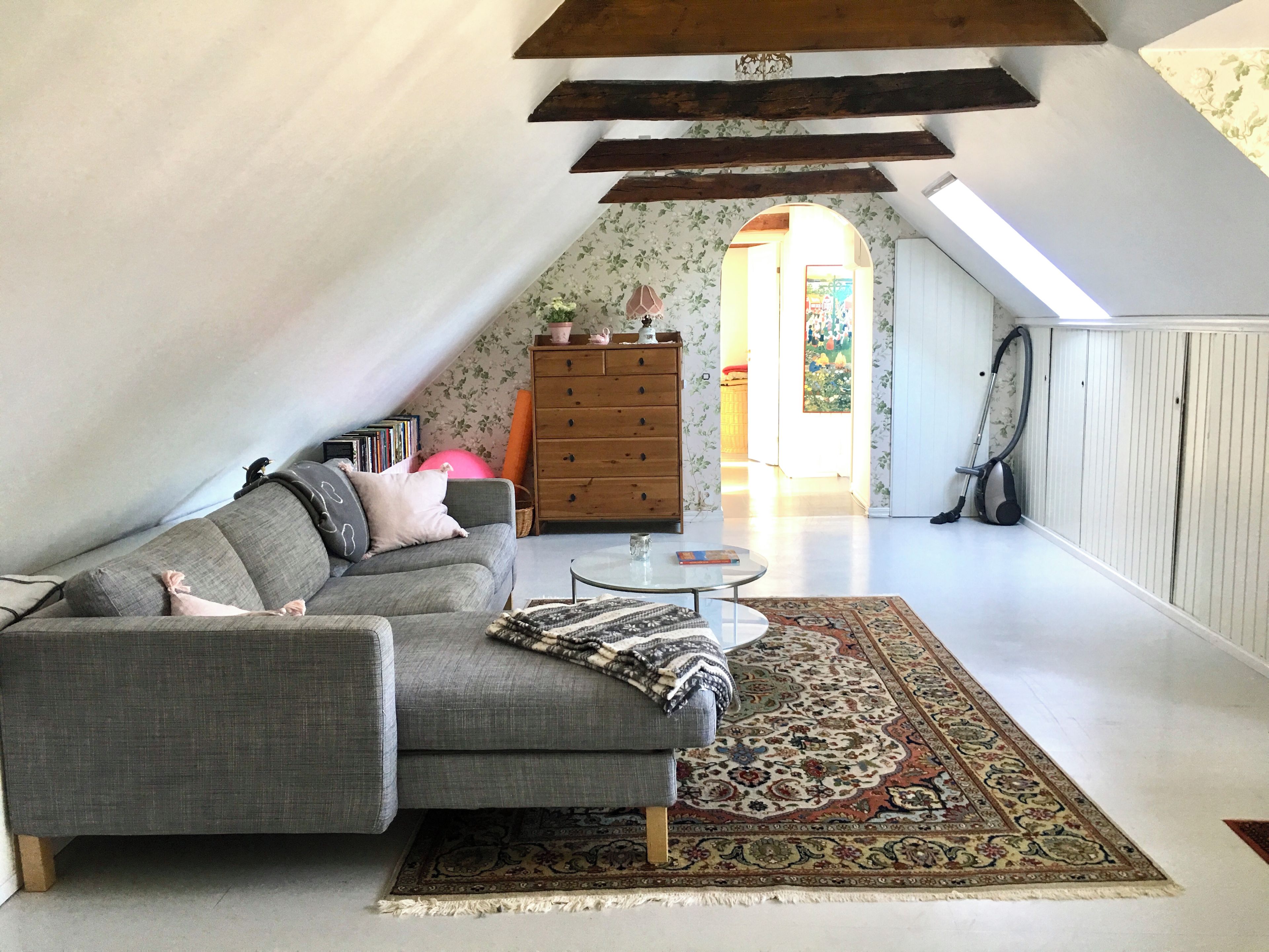A loft-style room with a grey sectional sofa, a small round table, and a patterned rug.