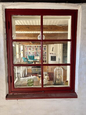 A room with a red-framed window, a wooden ceiling, and a bookshelf filled with books.