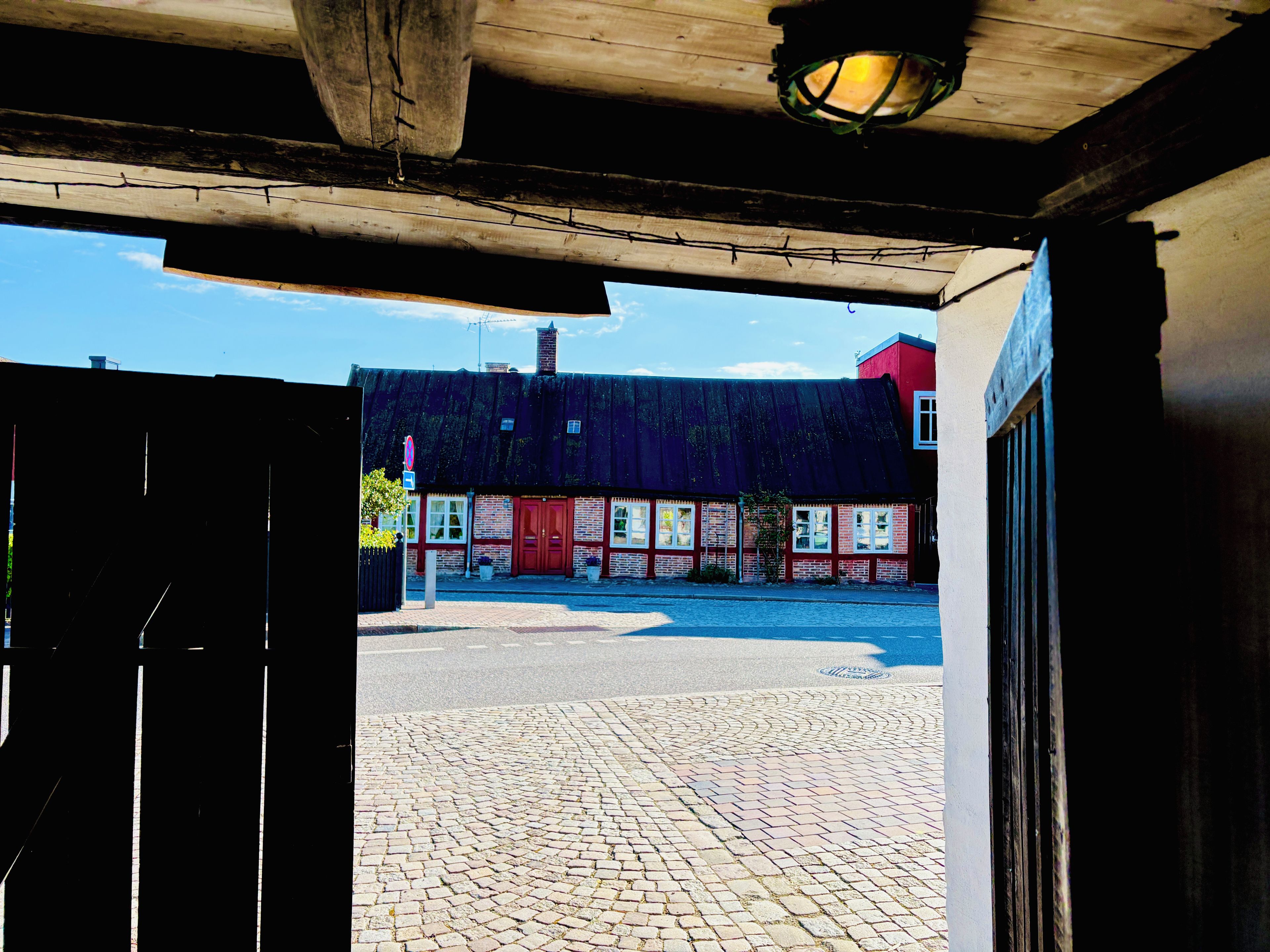 Une rue pavée menant à un bâtiment doté d’une porte rouge et d’un auvent noir.