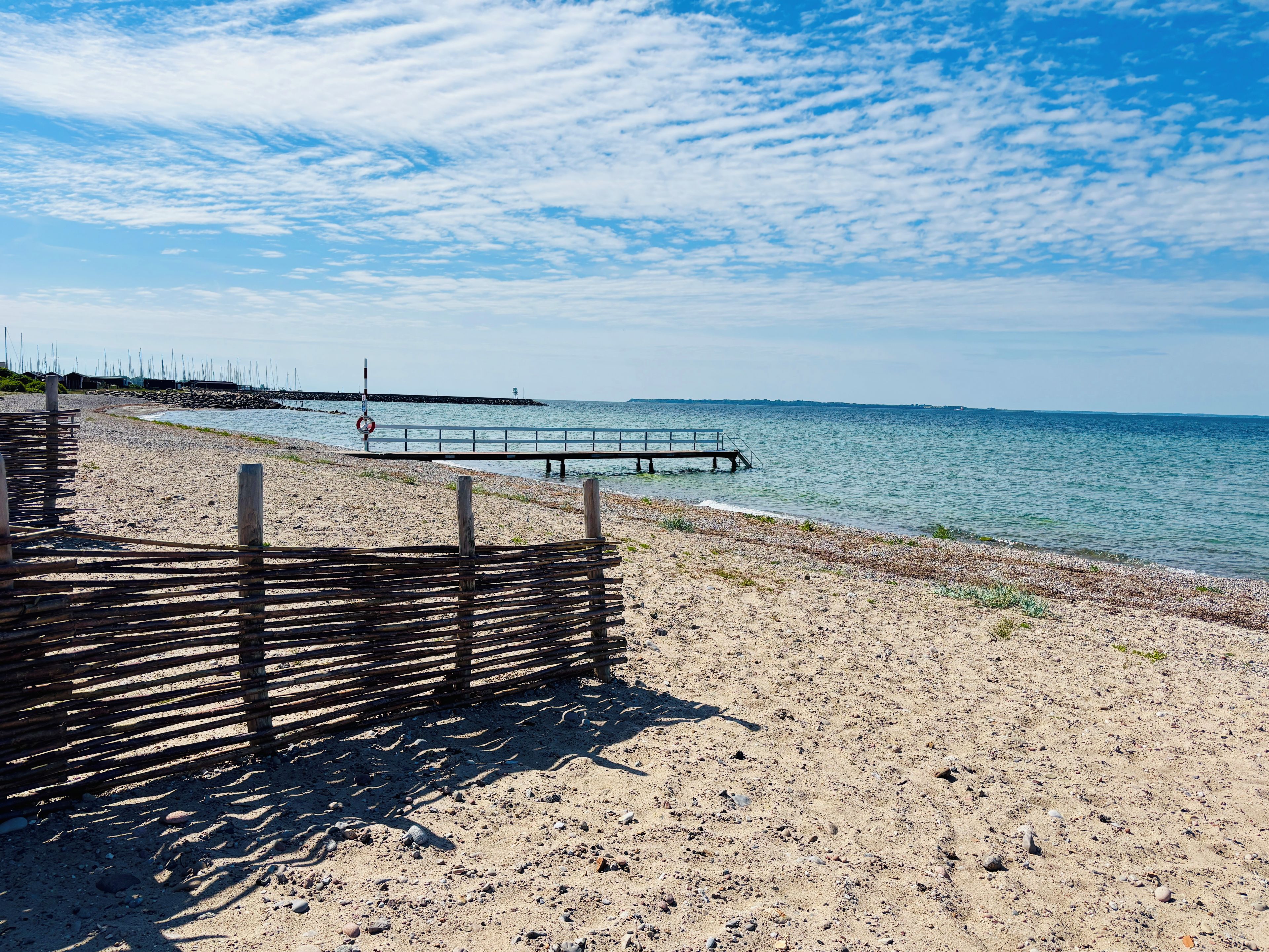 Una spiaggia con una recinzione di legno, un molo che si protende nell'acqua e un galleggiante di salvataggio.