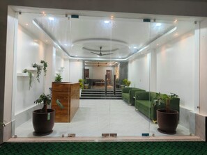 A reception area with a wooden desk, green sofas, potted plants, and a staircase leading to an upper level. - Majestic Inn (Guwahati)