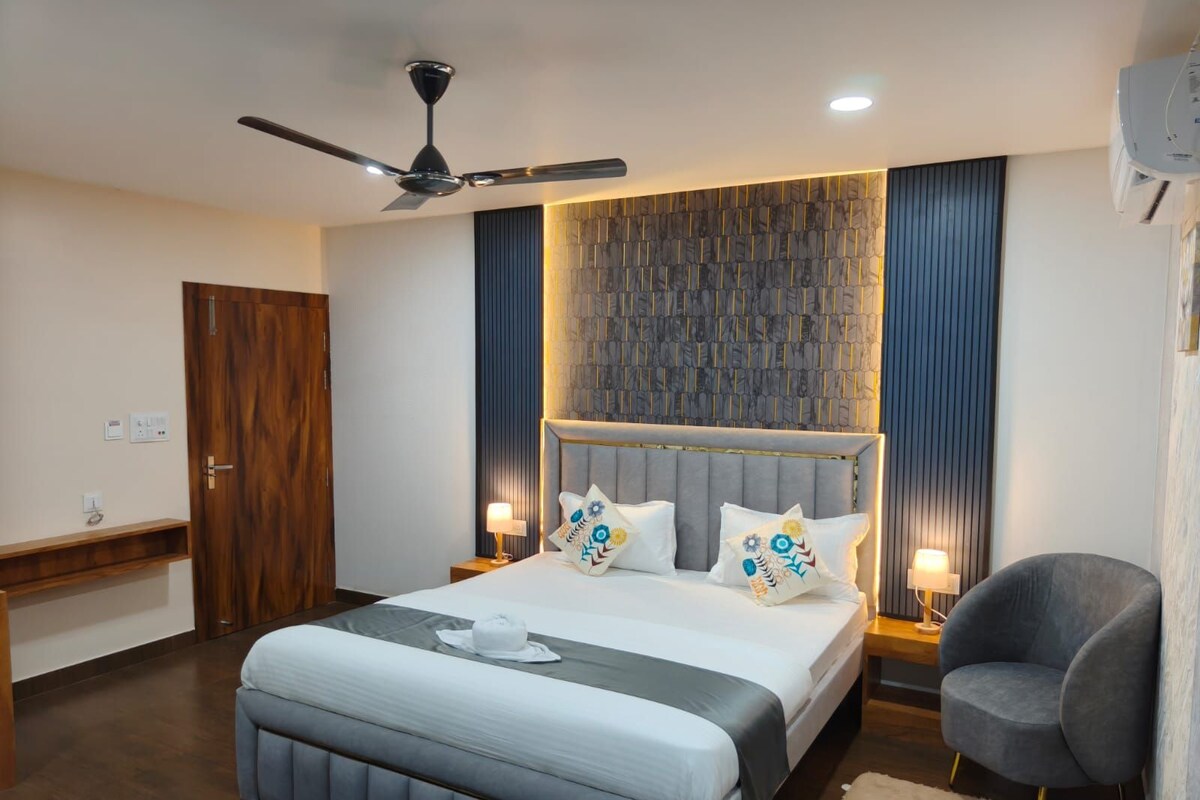 A modern bedroom with a large bed, a ceiling fan, a wall-mounted air conditioning unit, and a bedside table with a lamp.