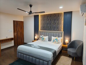 A modern bedroom with a large bed, a ceiling fan, a wall-mounted air conditioning unit, and a bedside table with a lamp. - Majestic Inn (Guwahati)
