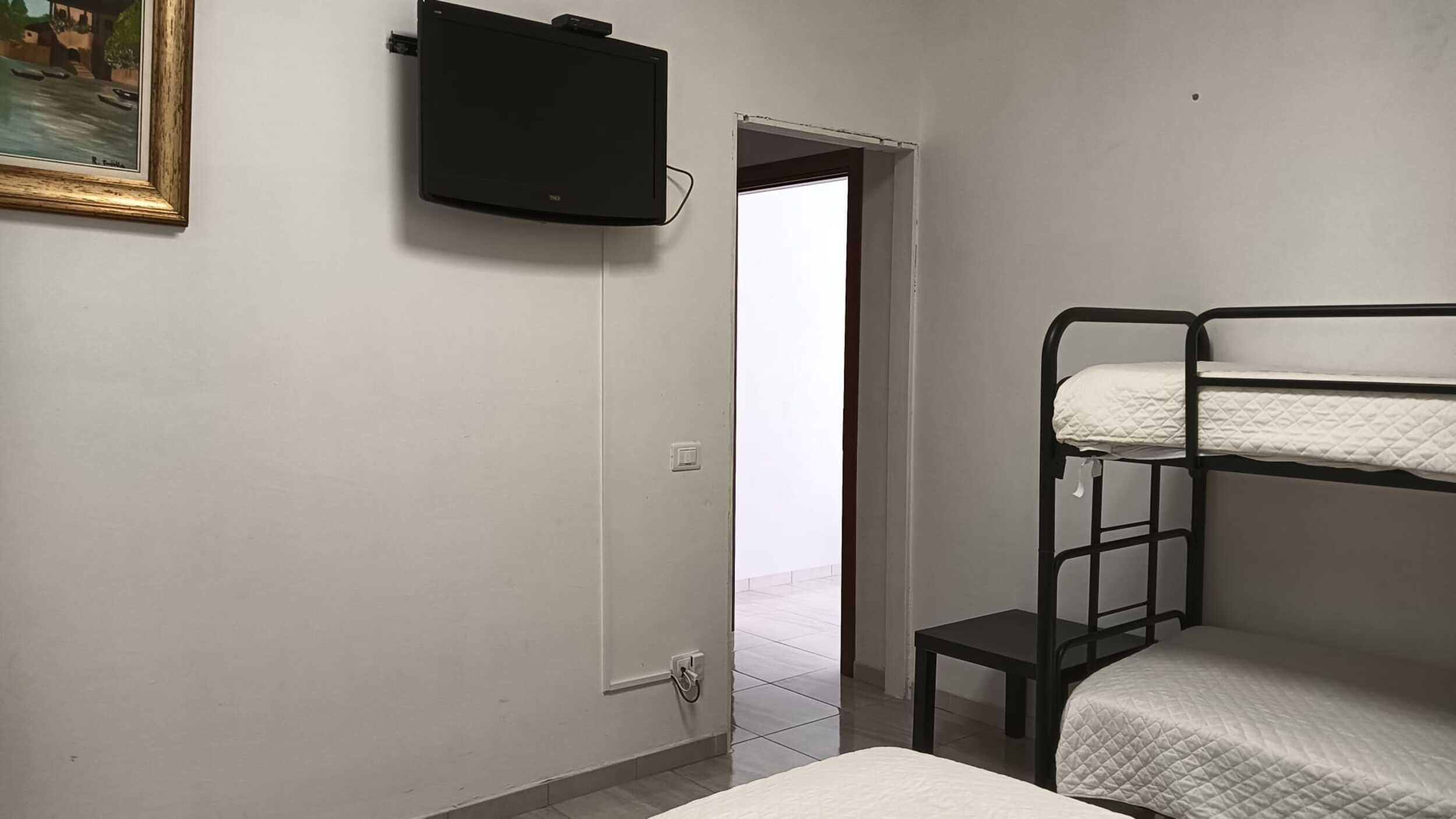 Une chambre avec des lits superposés, un téléviseur fixé au mur et une porte donnant sur un espace extérieur.