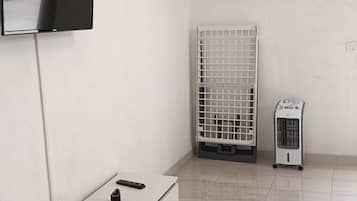 Une pièce dotée d’un téléviseur à écran plat fixé au mur, d’une armoire blanche avec des tiroirs, d’un radiateur, d’un chauffage d’appoint et d’un tableau encadré.