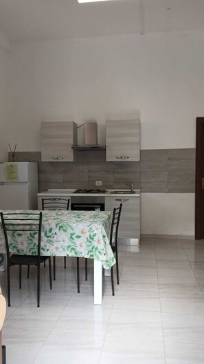 A modern kitchen with white cabinets, a gas stove, and a dining area with a table and chairs. - Apartment 'Pozzallo House' with Wi-Fi (Camerota)