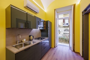 A modern kitchen with a sink, stove, and cabinets, leading to a balcony with a view. - Satriano Style Flat - Double Apartment (Naples)