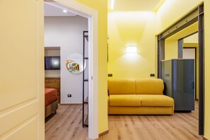 A room with a yellow sofa, a wooden floor, a TV, and a refrigerator. - Satriano Style Flat - Double Apartment (Naples)