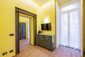 A hallway with a wooden floor, a grey cabinet with a television, and a sliding glass door. - Satriano Style Flat - Double Apartment (Naples)
