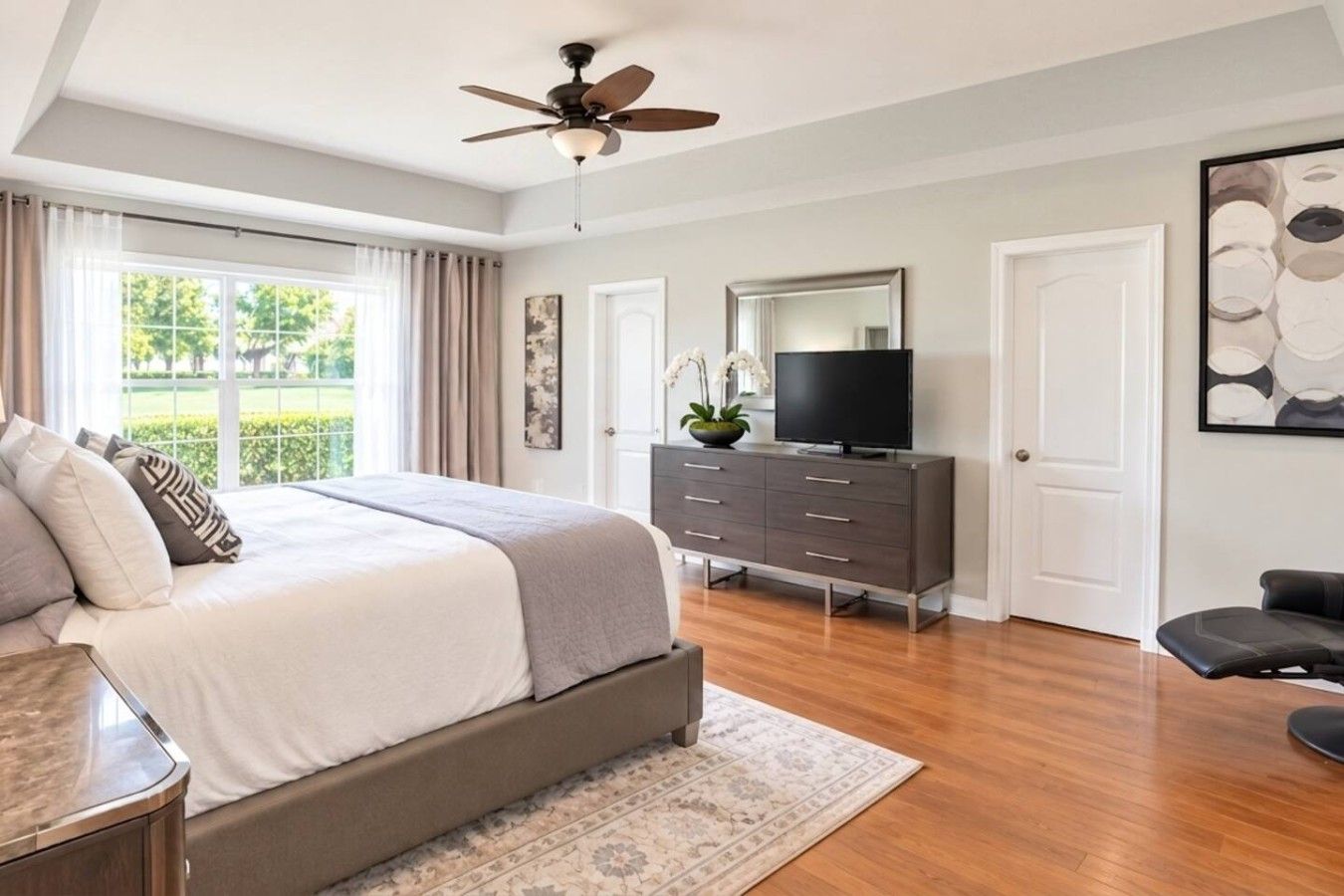 Une chambre à coucher comprenant un lit, une commode, un téléviseur et un ventilateur de plafond.