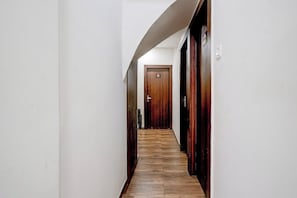 Un pasillo estrecho con piso de madera y paredes blancas, que conduce a una puerta con el número 103.