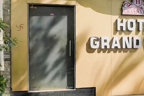 Una puerta metálica cerrada con un pequeño ventanal, un cartel que dice 'HOT GRAND' en la pared y una vista parcial del exterior de un edificio.