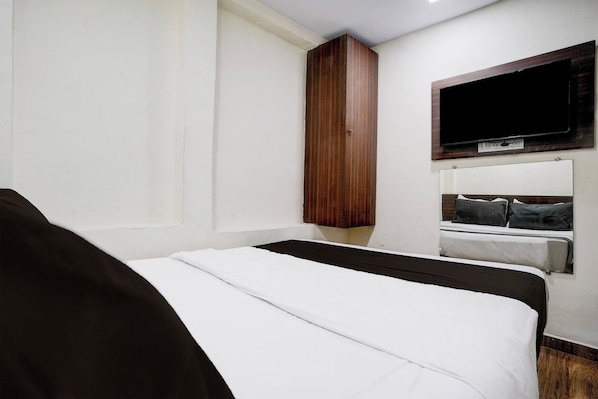 Un dormitorio con cama, armario de madera, televisor montado en la pared y ventana.