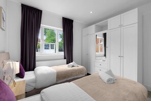 Une chambre d’hôtel avec deux lits, une grande armoire, un miroir et une fenêtre avec des rideaux.