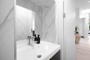 Une salle de bain moderne avec un lavabo en marbre blanc, un grand miroir et une plante en pot.