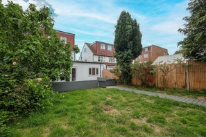Un jardin à l’arrière d’une maison, avec une pelouse, une clôture en bois et un grand arbre.