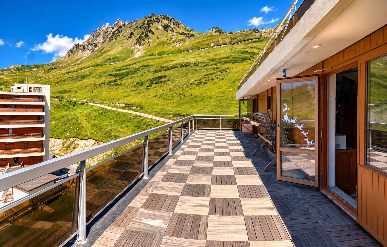 Een terras met een zwart-wit geruite vloer, een leuning en uitzicht op een bergachtig landschap.