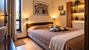 Un dormitorio con cama, lámparas de noche, un collage enmarcado en la pared y un radiador.