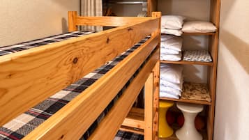 A bunk bed with a plaid-patterned mattress, a wooden headboard, and a shelf with folded towels and pillows.