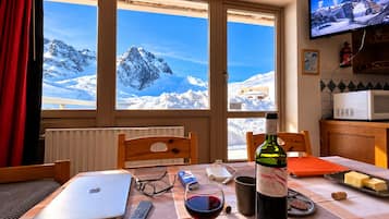 Un comedor con una mesa preparada para dos personas, una laptop, una copa de vino, controles remotos y una botella de vino.