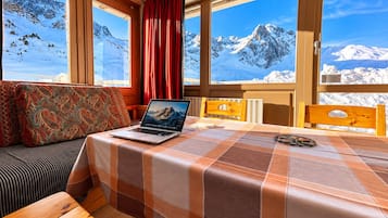 Una habitación con cama, una laptop sobre la cama, una ventana con vista a la montaña y una cortina roja.