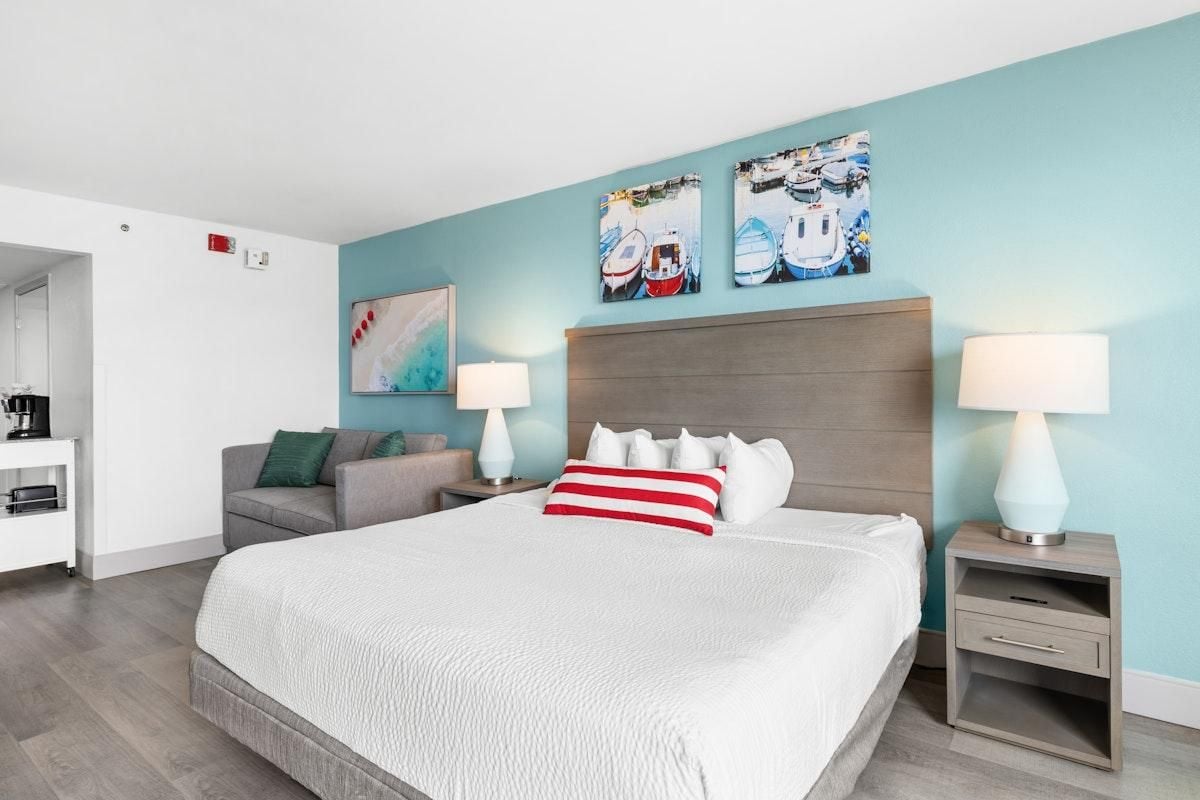 A hotel room with a large bed, two bedside tables with lamps, a sofa, and artwork on the walls.