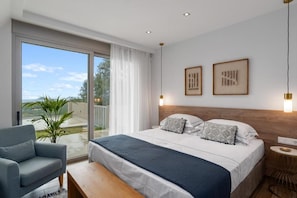 Ein modernes Schlafzimmer mit einem großen Bett, einer Couch, einem kleinen runden Tisch und Blick durch eine Schiebetür.