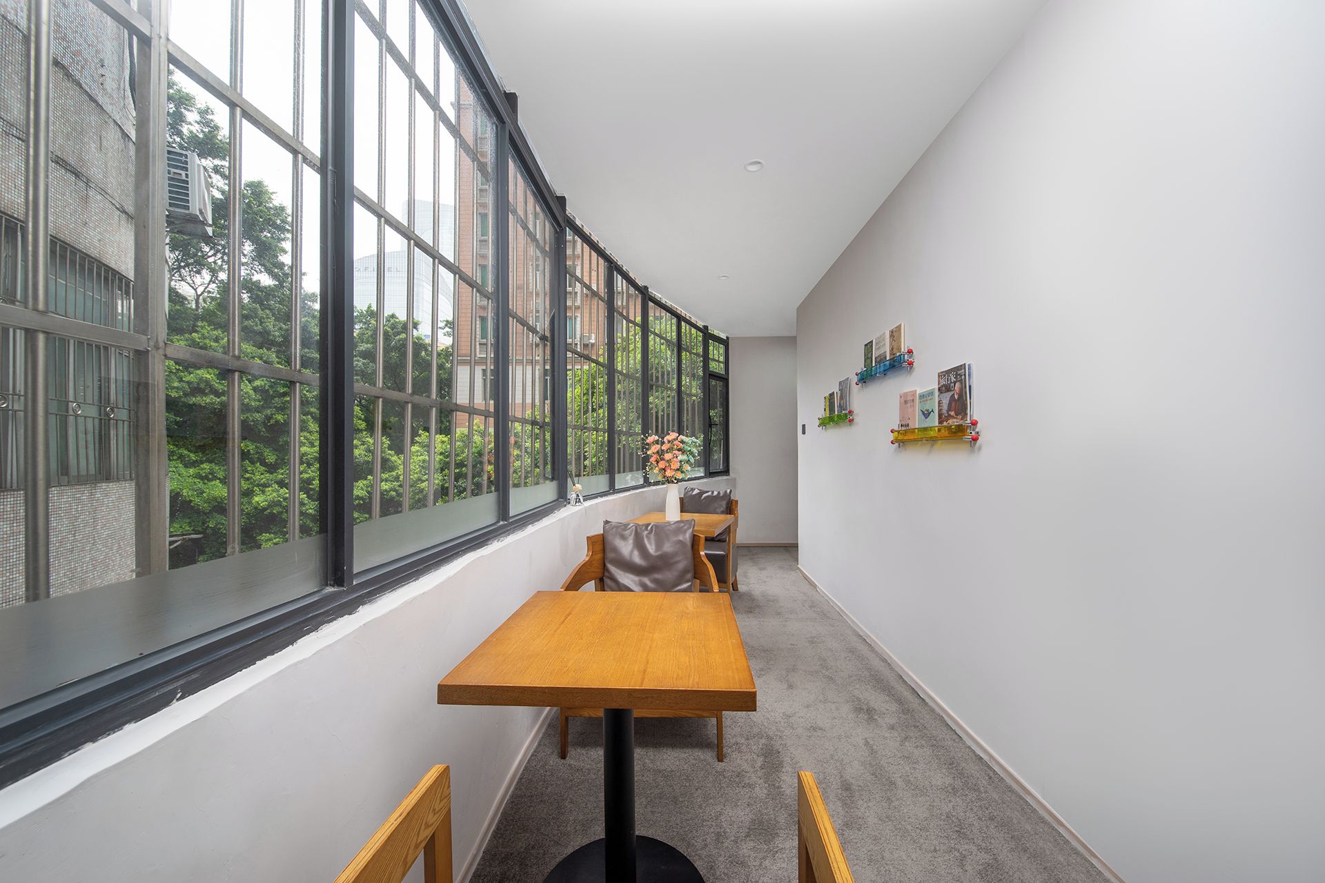 A corridor with a wooden table and chairs, a window with a view of trees, and a wall with framed pictures.