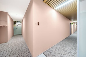 A corridor with a patterned floor, a wall-mounted intercom, and a door with a green sign. - Litchi in Red - outh Stay Inn (Guangzhou)