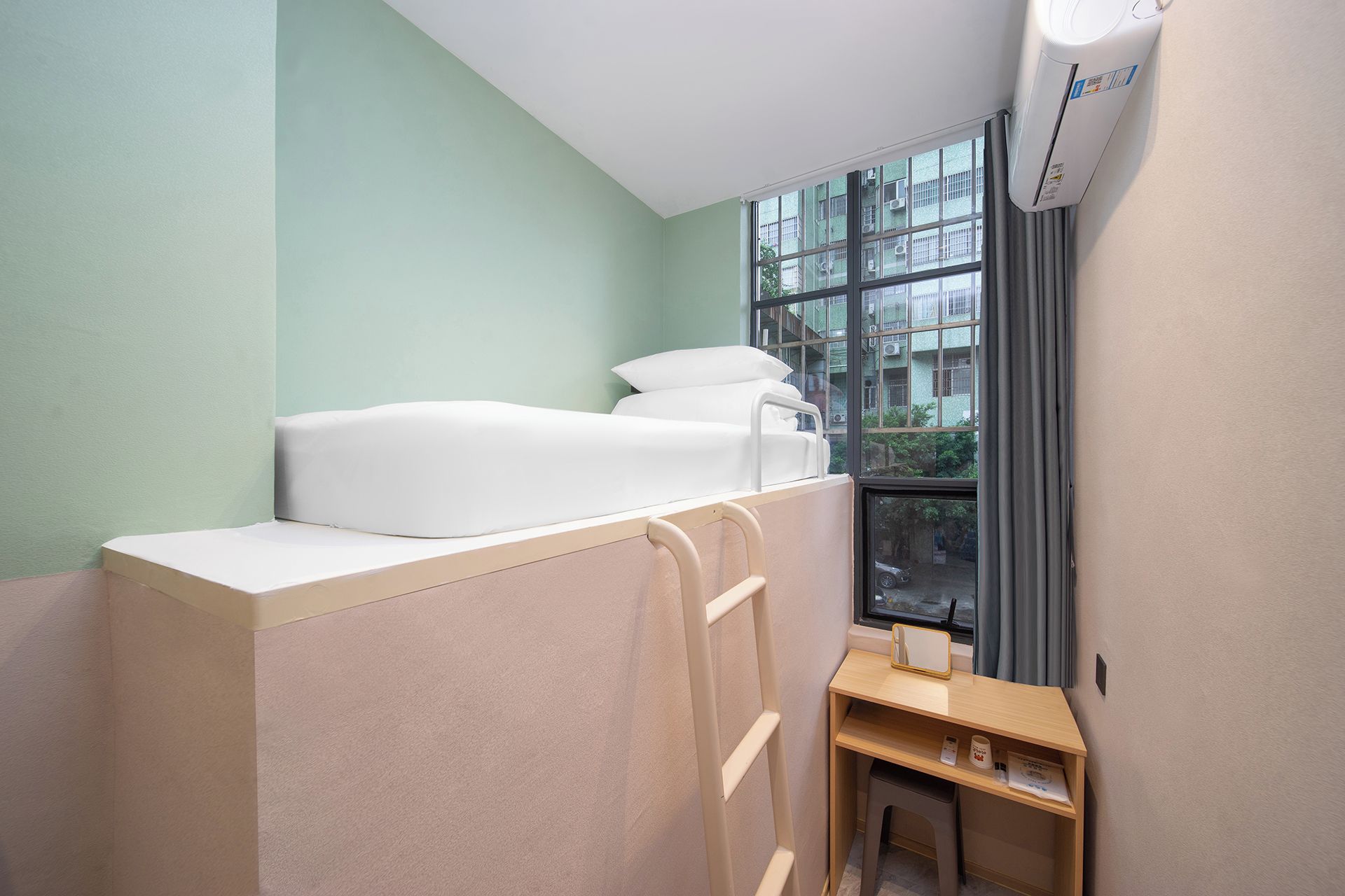 A room with a bunk bed, a small desk with a mirror, and a window with a view of buildings.