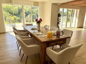 Un coin repas avec une table en bois, six chaises et une grande fen être donnant sur un paysage verdoyant.