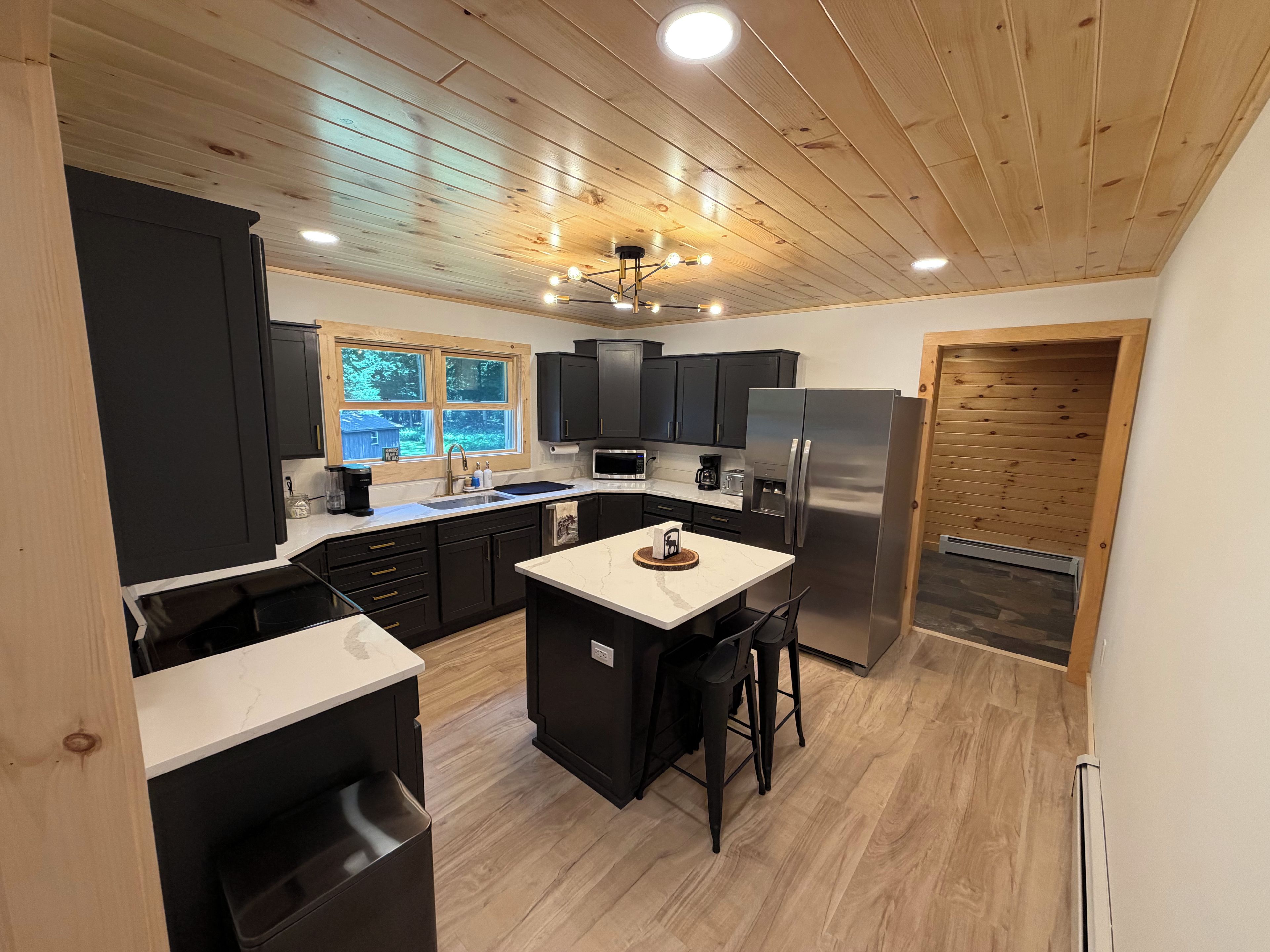 A modern kitchen with a central island, black cabinetry, and a wooden ceiling.