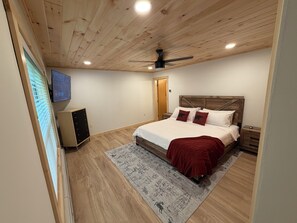 A bedroom with a wooden ceiling, a bed with white bedding and red pillows, a television on the wall, and a wooden cabinet. - NEW TASTEFULLY UPDATED RUSTIC CAMP WATERFRONT! IN OLD FORGE (Old Forge)