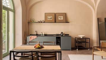 A dining area with a table set for two, a kitchen with a built-in island, and framed pictures on the wall.