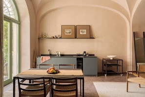 A dining area with a table set for two, a kitchen with a built-in island, and framed pictures on the wall. - Serra Novecento Garden Suite & Residence _La Veranda_ (Bellano)